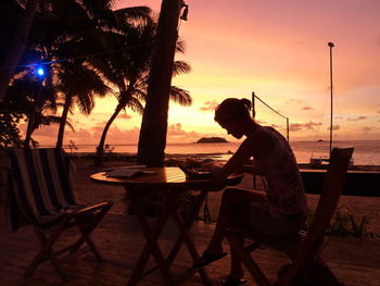 Woman sitting on table at beach during sunset