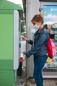 Side view of woman wearing mask standing by ticket machine