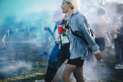 Friends enjoying drinks while walking amist powder paint in festival