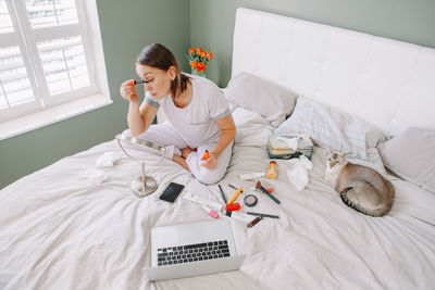 Woman doing make up while sitting on bed at home