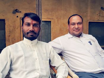 Portrait of smiling men wearing white shirts while sitting against house