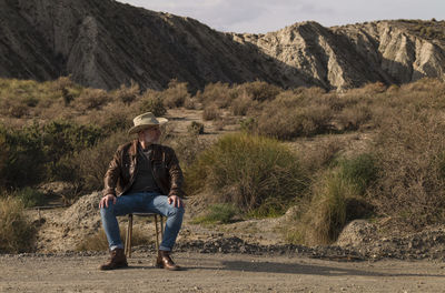 Adult man in cowboy hat sitting on abandoned chair in desert, almeria, spain