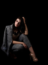 Portrait of young woman sitting against black background