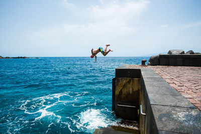 Man jumping on sea against sky