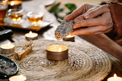 Woman hands burning white sage, before ritual on the table with candles and green plants. smoke of