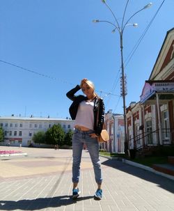 Low angle view of mid adult woman eating lollipop while standing on street against clear blue sky