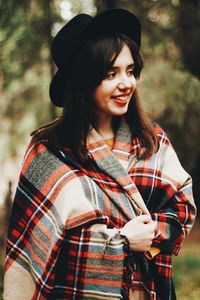 Smiling young woman wrapped in blanket looking away at park