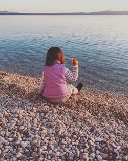 Rear view of woman sitting on rocks at beach