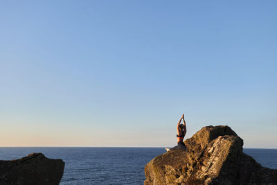 Rear view of man standing on rock by sea against clear sky