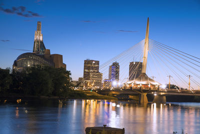 Illuminated buildings by river against sky in city