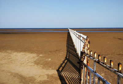 Wooden railing on beach against clear sky