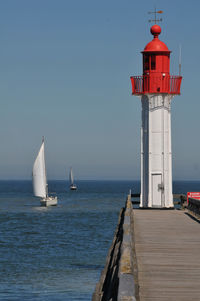 Lighthouse on pier by sea against sky