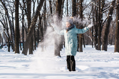 Happy girl in warm clothes rejoices in the snow in the winter park. walk outdoors.