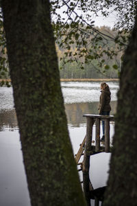 Woman standing on tree by lake against sky
