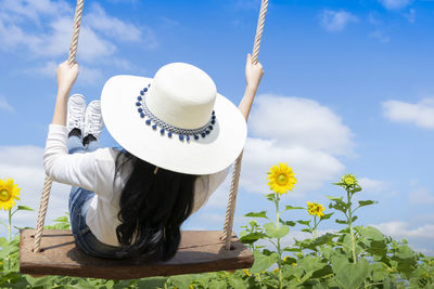 Rear view of woman sitting on swing in field