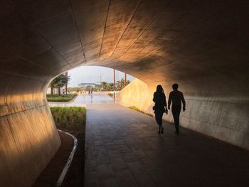 Rear view of people walking on footpath in tunnel