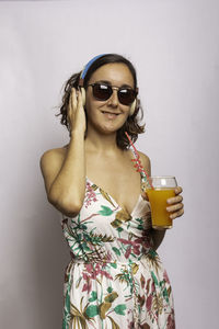 Portrait of young woman wearing sunglasses standing against white background