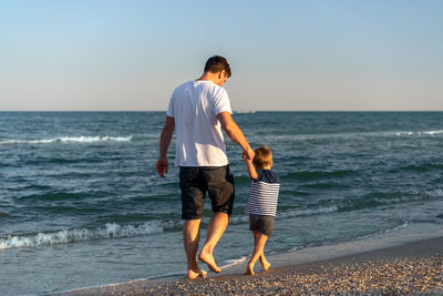 View of father and son on beach against sky