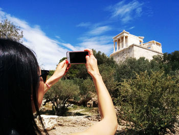 Woman photographing parthenon temple against sky