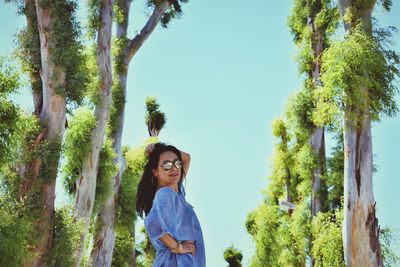 Woman standing by tree trunk against sky