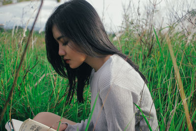 Side view of young woman reading book while sitting on grass