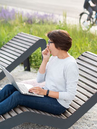 Woman with laptop on park bench.freelancer yawns at work. student learns remotely. modern lifestyle.