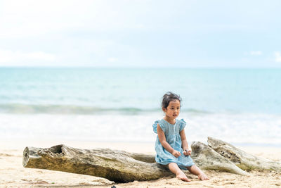 Full length of man sitting on rock at beach against sky