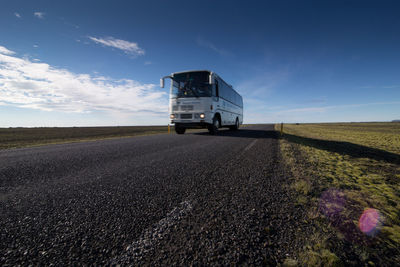 Bus moving on road amidst landscape against sky