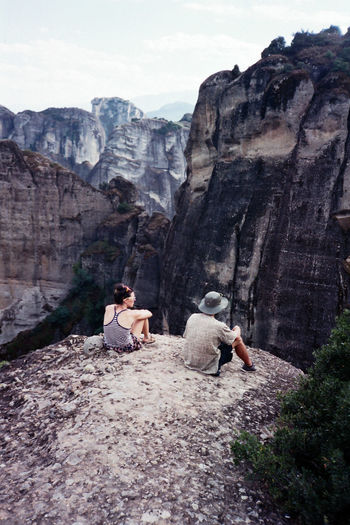 Rear view of man and woman sitting on rock against mountains