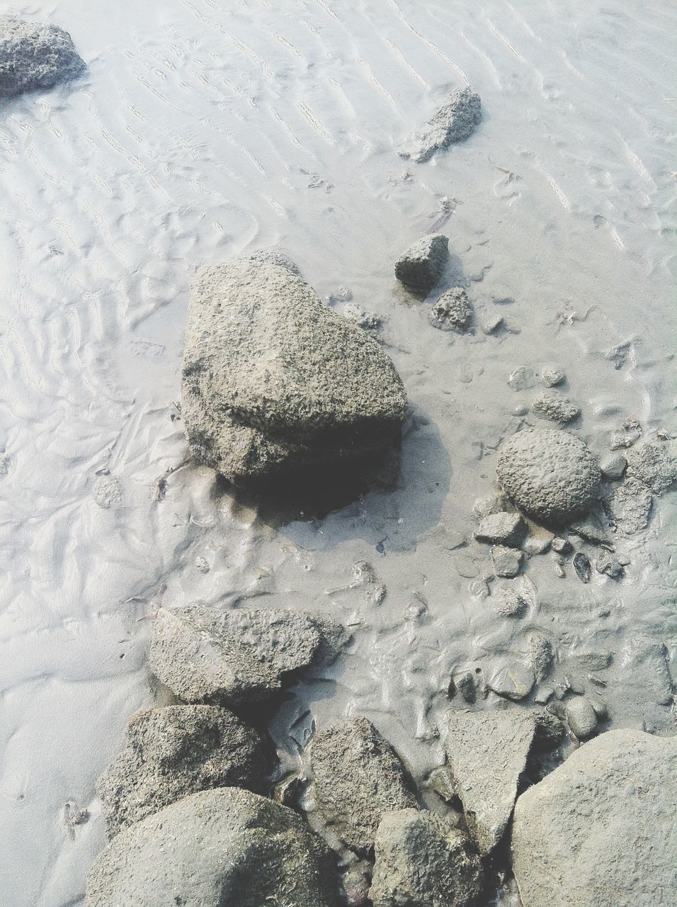 beach, sand, shore, high angle view, water, nature, pebble, stone - object, tranquility, sea, day, textured, rock - object, sunlight, footprint, wet, outdoors, beauty in nature, surf, no people