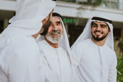 Smiling senior man with grandsons wearing dish dash sitting outdoors