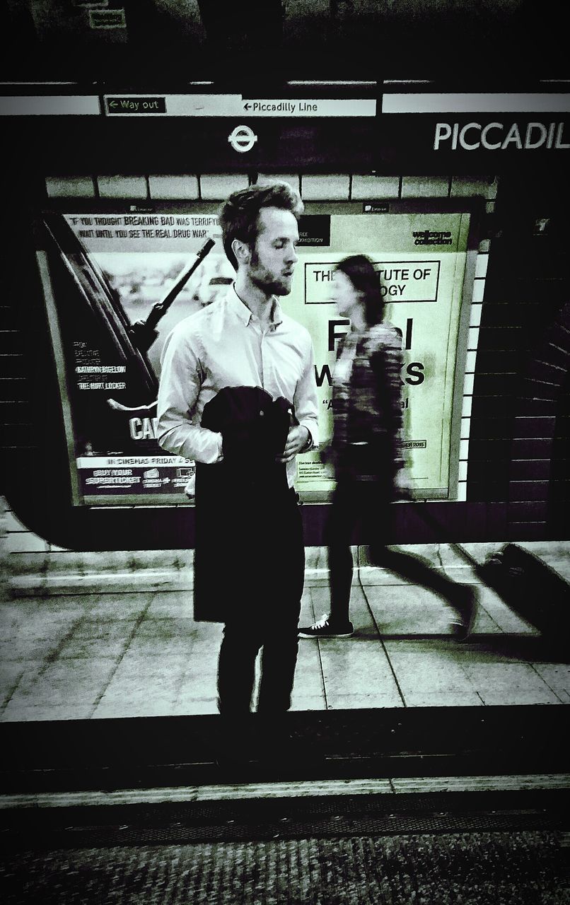 REAR VIEW OF MAN WALKING ON RAILROAD STATION PLATFORM