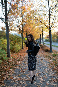 Portrait of woman holding flower on sidewalk during autumn