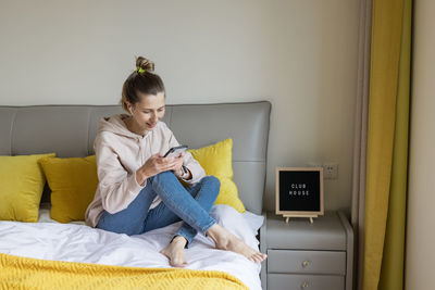 Side view of boy using mobile phone while sitting on bed at home