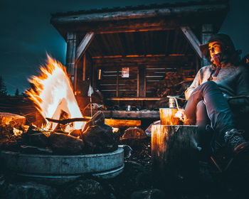 Young man sitting by campfire outdoors