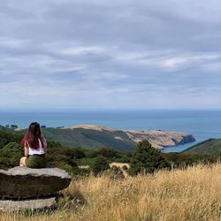 Rear view of woman sitting on land against sky