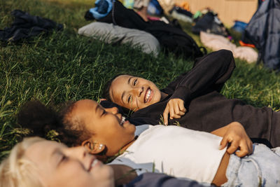 Happy girl enjoying with friends while lying down on grass at summer camp