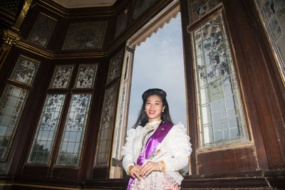 Portrait of smiling young woman in traditional clothing standing by window