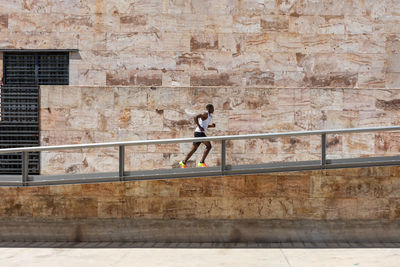 Side view of african american male athlete running along metal construction in street during active training