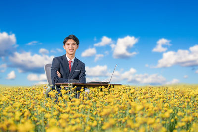 Portrait of smiling businessman sitting with laptop on field