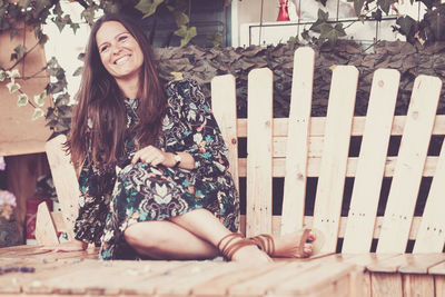 Full length of smiling woman sitting on wooden bench