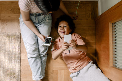 Directly above shot of happy siblings using smart phones on hardwood floor at home