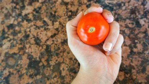 Cropped hand of woman holding fresh tomato over marble