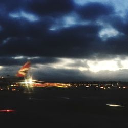 Airplane flying over illuminated city against sky at night