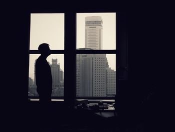 Rear view of silhouette woman looking through window