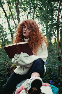 Young woman sitting by tree against plants