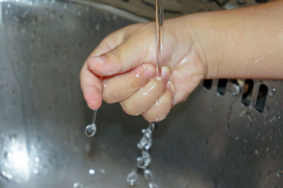Close-up of hand holding water falling from faucet