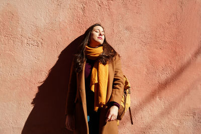 Young woman looking away while standing against wall