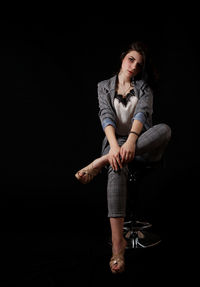 Full length of young woman sitting against black background