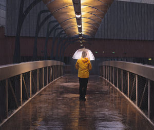 Rear view full length of woman with umbrella standing in footbridge during rainy season at night